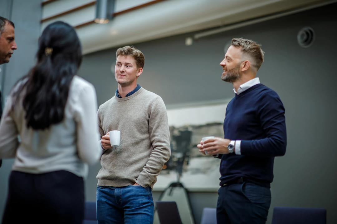 En gruppe mennesker snakker sammen med kaffe i hånden