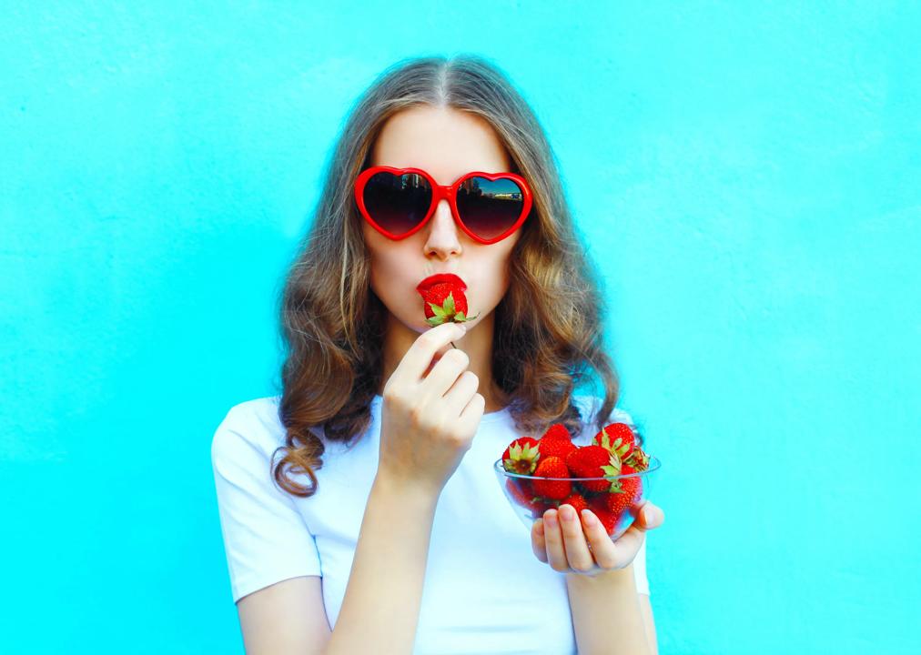 A woman with sunglasses eating a strawberry.