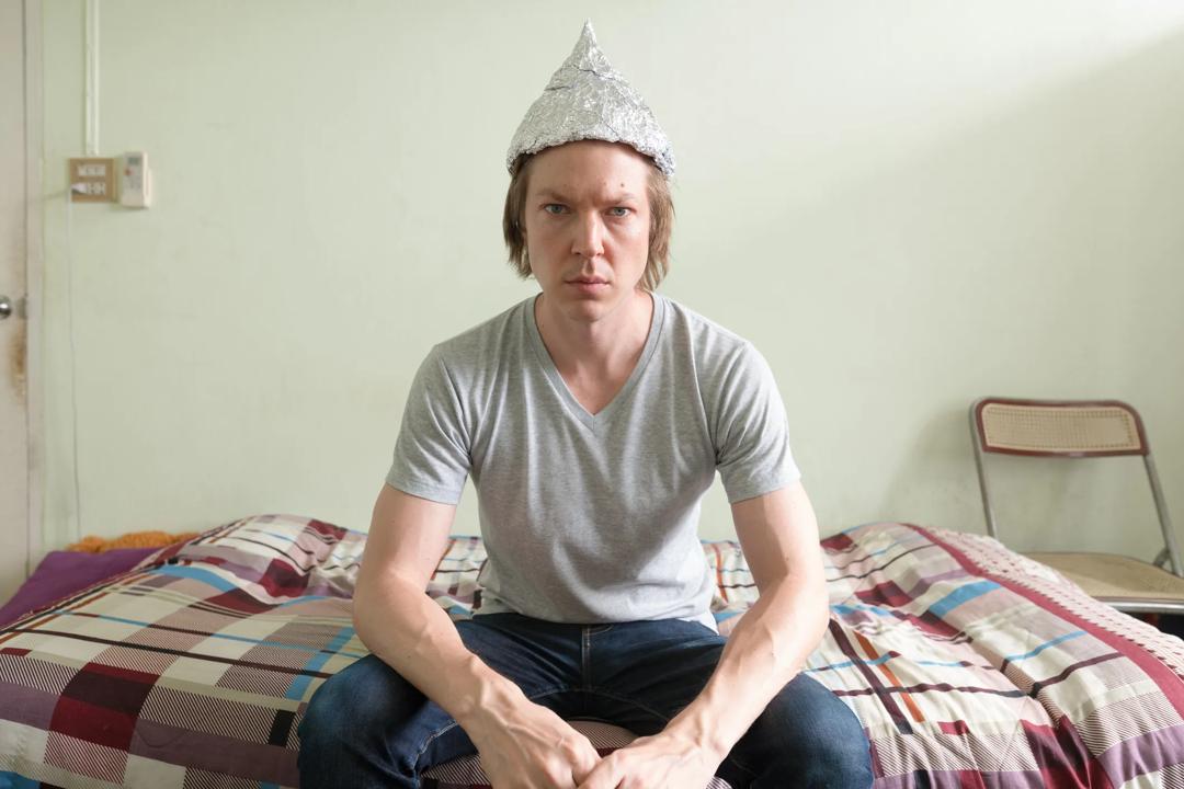 Young man on bed wearing tin foil hat
