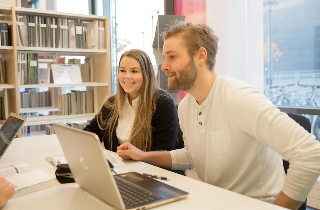 Studenter som sitter på å jobber på en pc, på et bibliotek