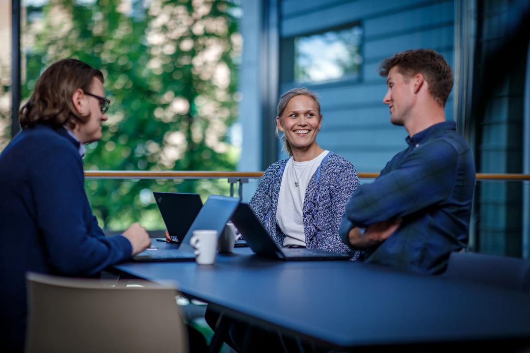 Tre personer som snakker sammen rundt et bord.