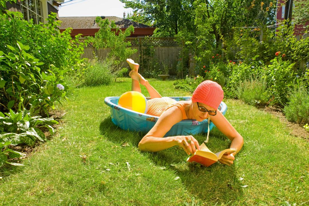 Woman laying in a kids pool reading a book