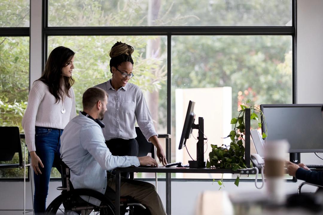Tre personer som ser på en pc sammen på et kontor.