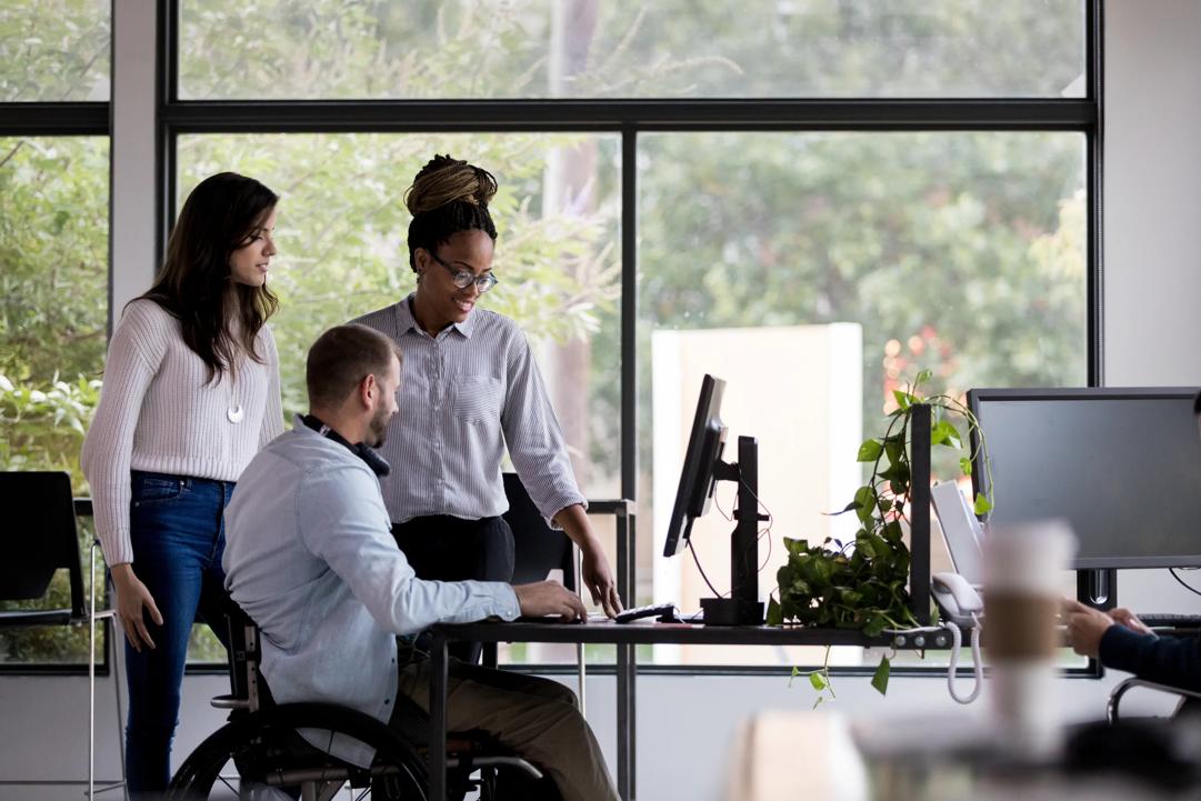 Tre personer som ser på en pc sammen på et kontor.