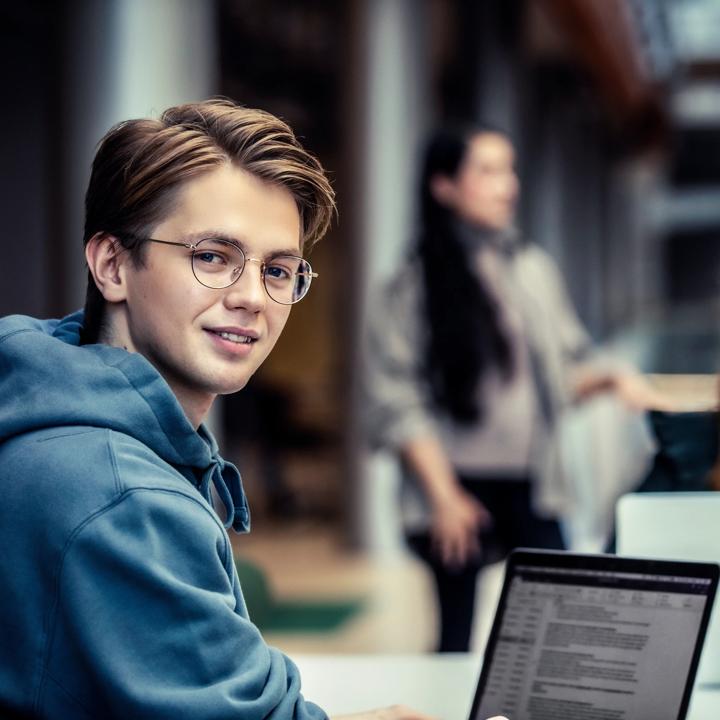 Mannelig student som ser mot kamera foran en kvinne som studerer