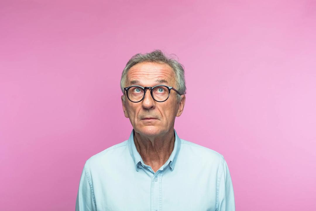Usikker og tankefull mann foran rosa bakgrunn.