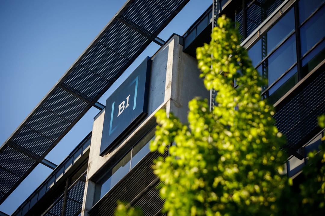 Utenfor campus Oslo på Nydalen. Bildet er zoomet inn på BI-logoen på bygget med et grønt tre ved siden av seg.