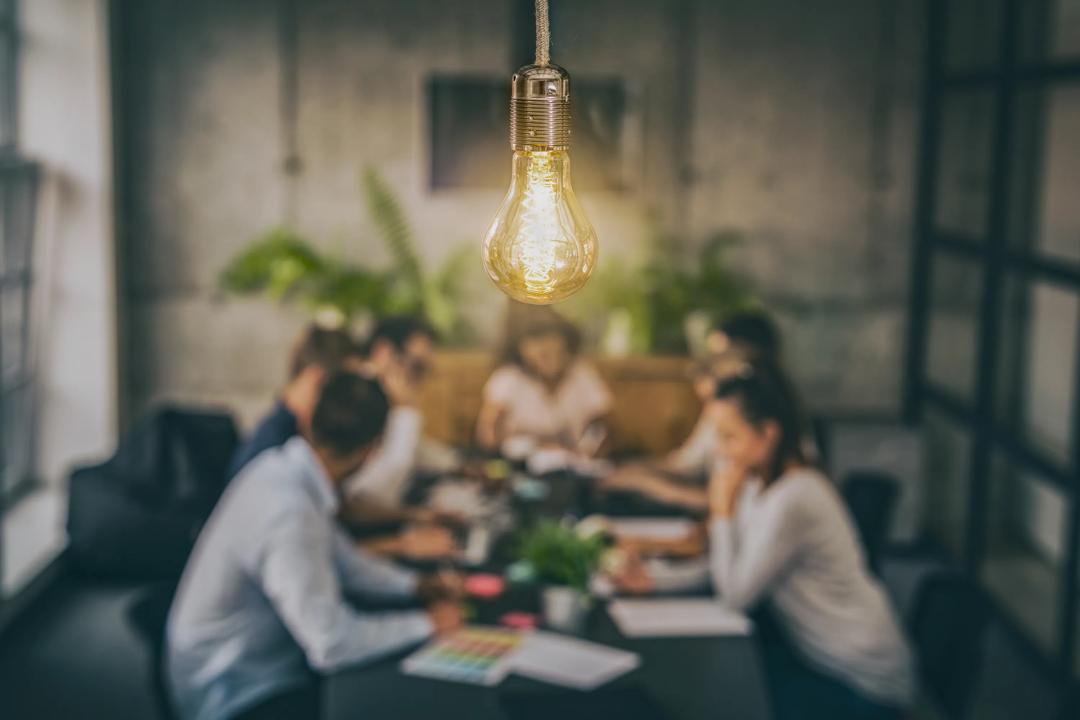 Group of people sitting together and working. A light bulb in focus.