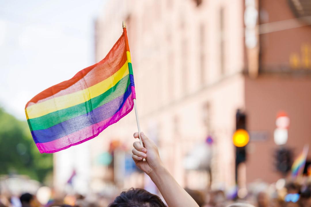 Bilde av en hånd som holder Pride-flagget i toget