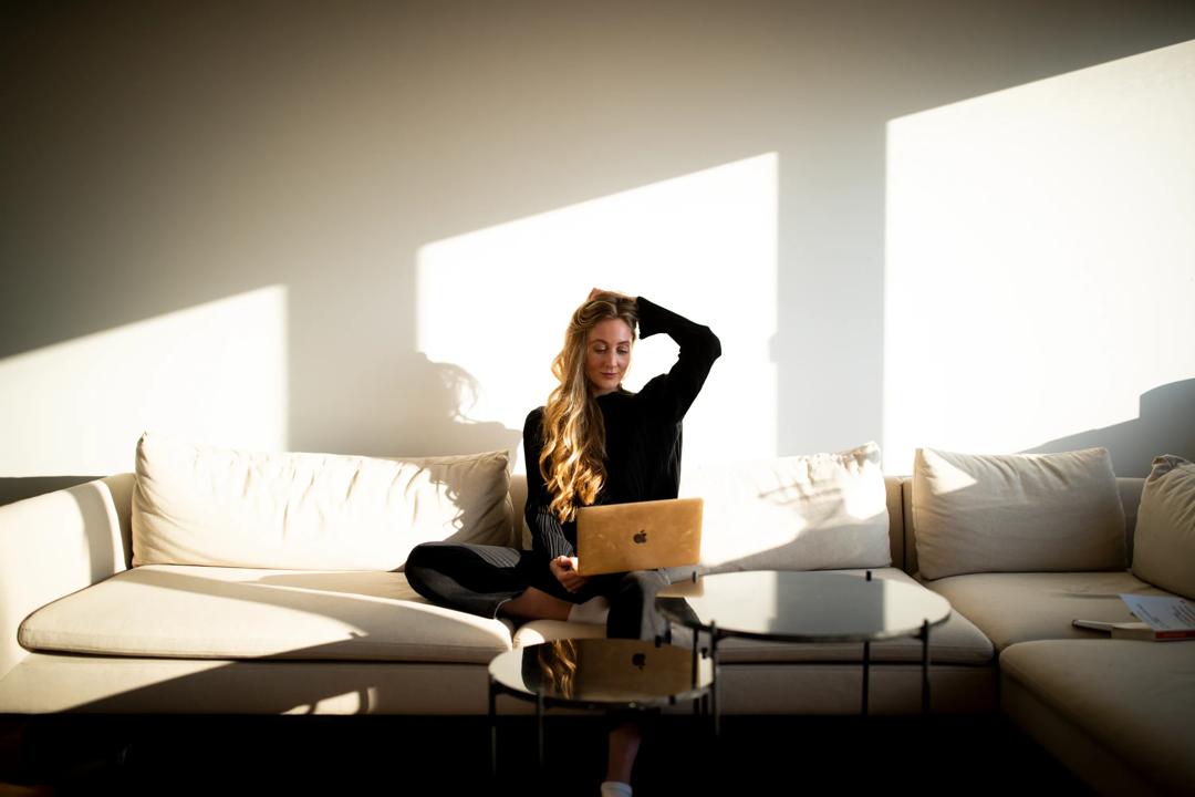 Rita Haugeland som sitter p&aring; en sofa og ser p&aring; pc-en sin