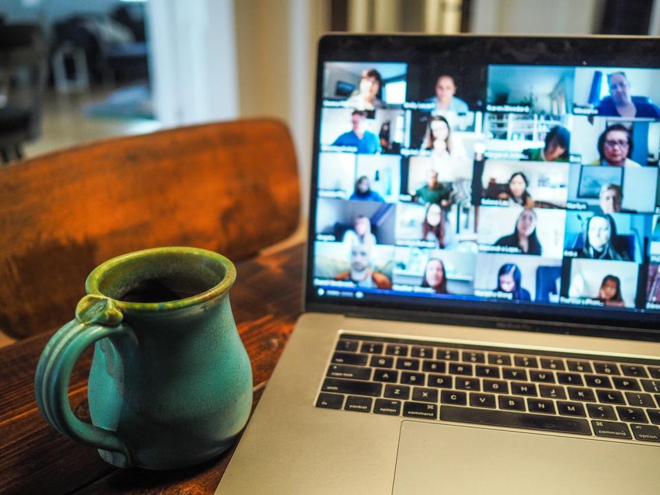 IImage of an online meeting. A pc screen with attendees from the online meeting and a coffee beside the PC.