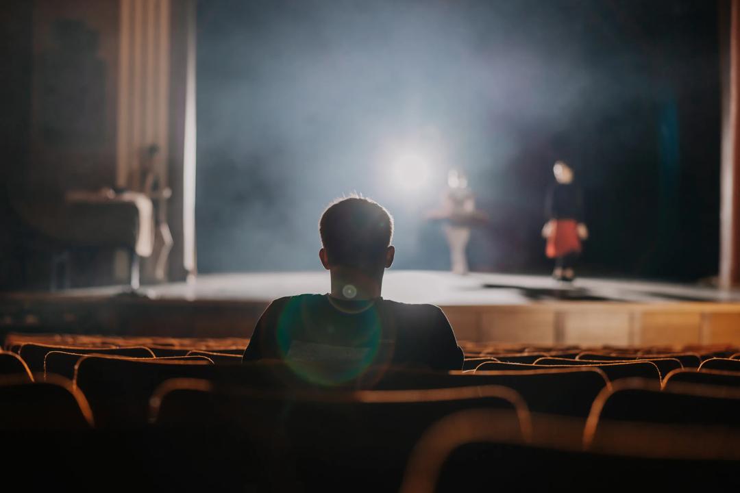 Man sitting in a theatre looking at bright stage