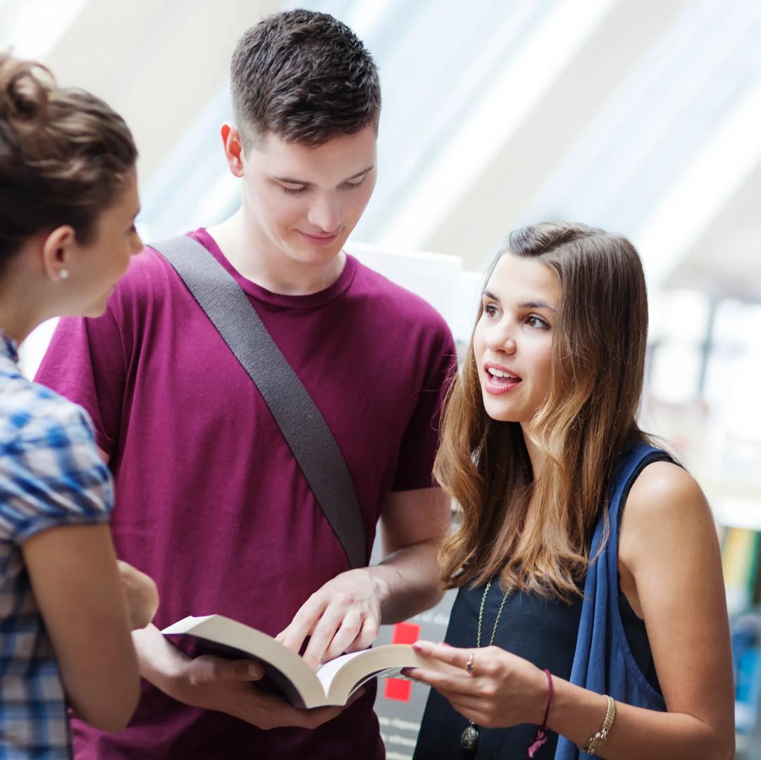 Tre studenter peker på en åpen bok