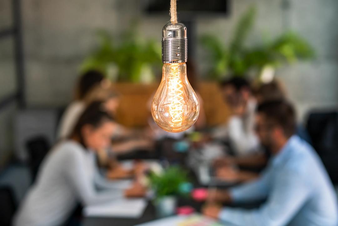 A group of people working around a table. A light bulb is in focus.