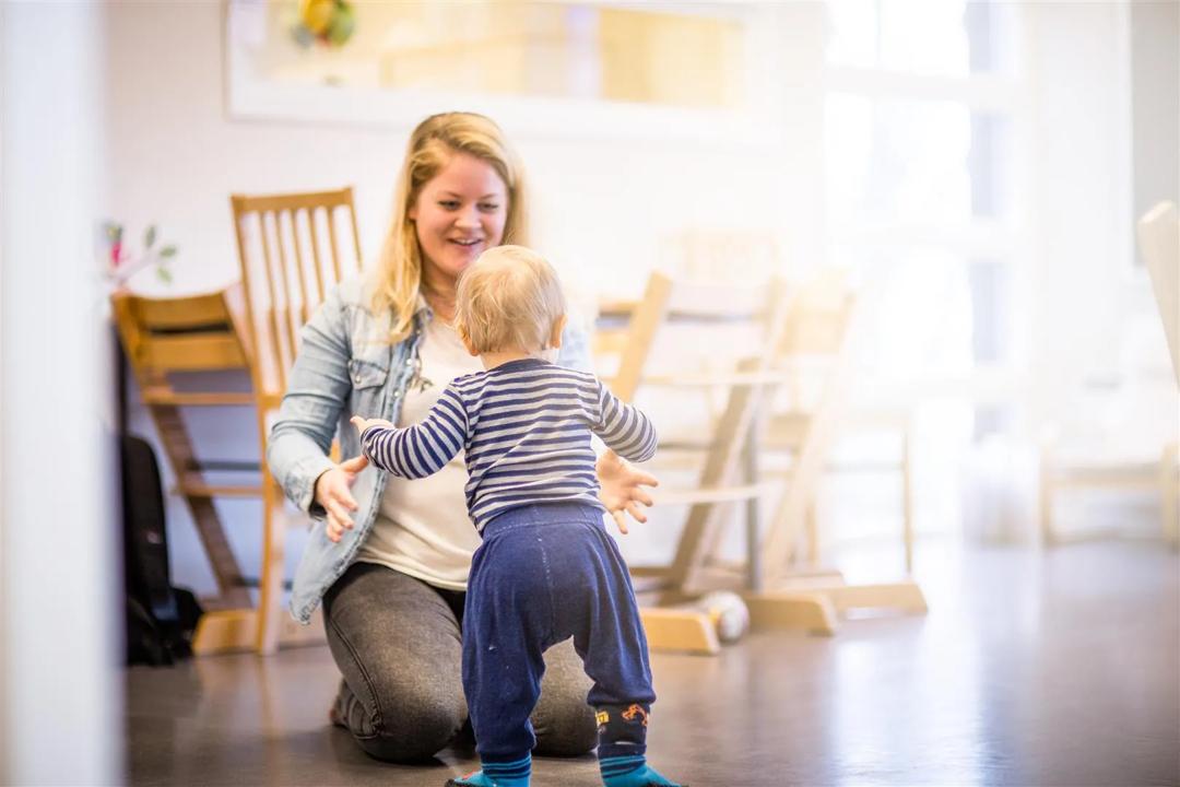 Barnhage ansatt som tar imot et barn som går mot henne