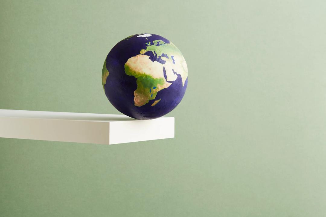 Earth about to fall off a plank set against a green backround