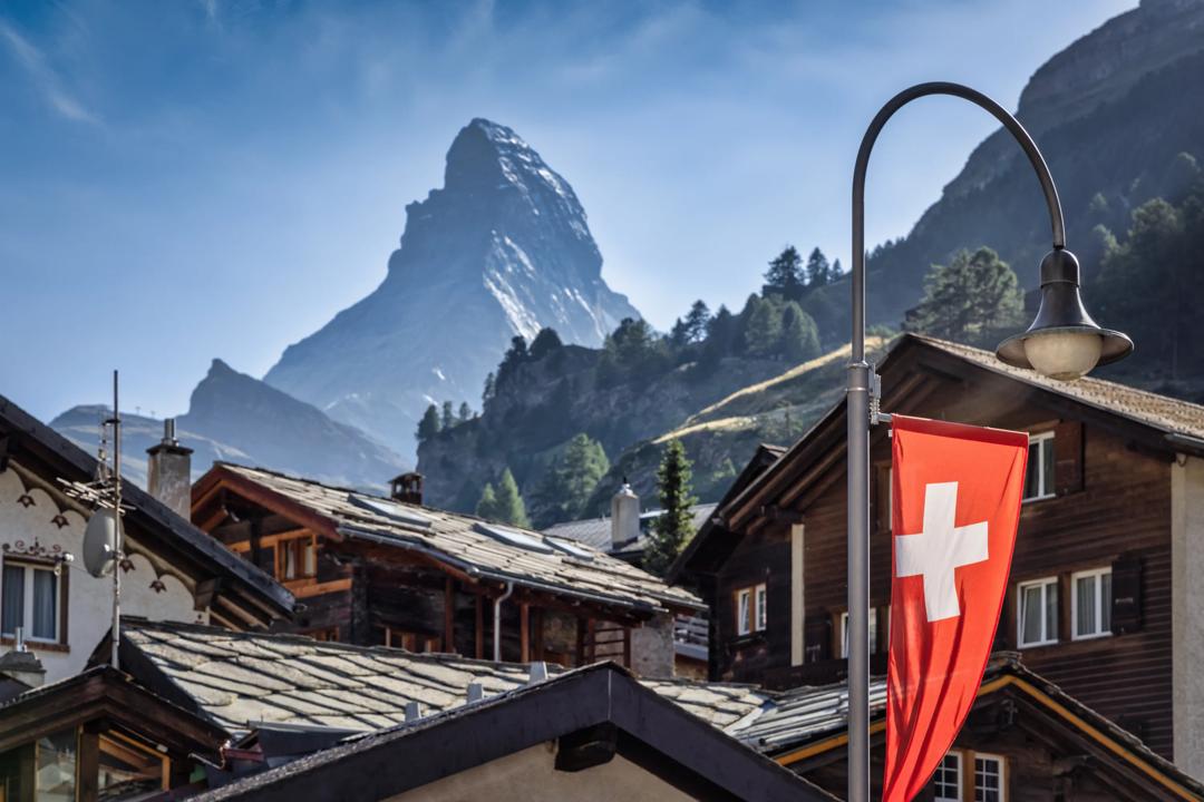 Swiss flag set against a village with Matterhorn in the background.