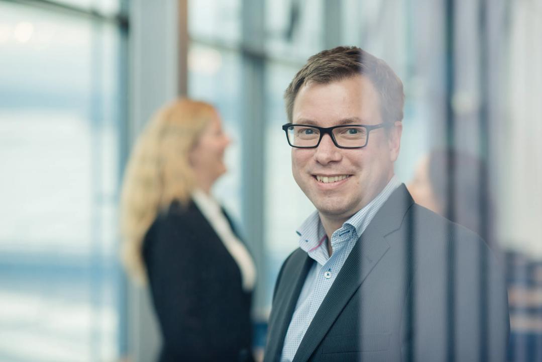 Smilende mann som står foran to damer som snakker sammen