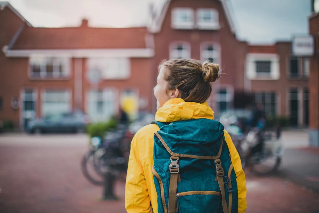 En jente med gul regnjakke og sekk som ser utover