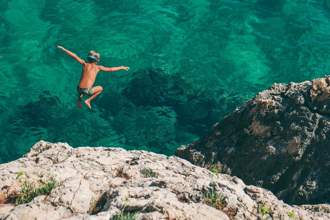 Bilde av gutt som stuper i grønt vann. (Foto: Nikola Radojcic, Unsplash.com).