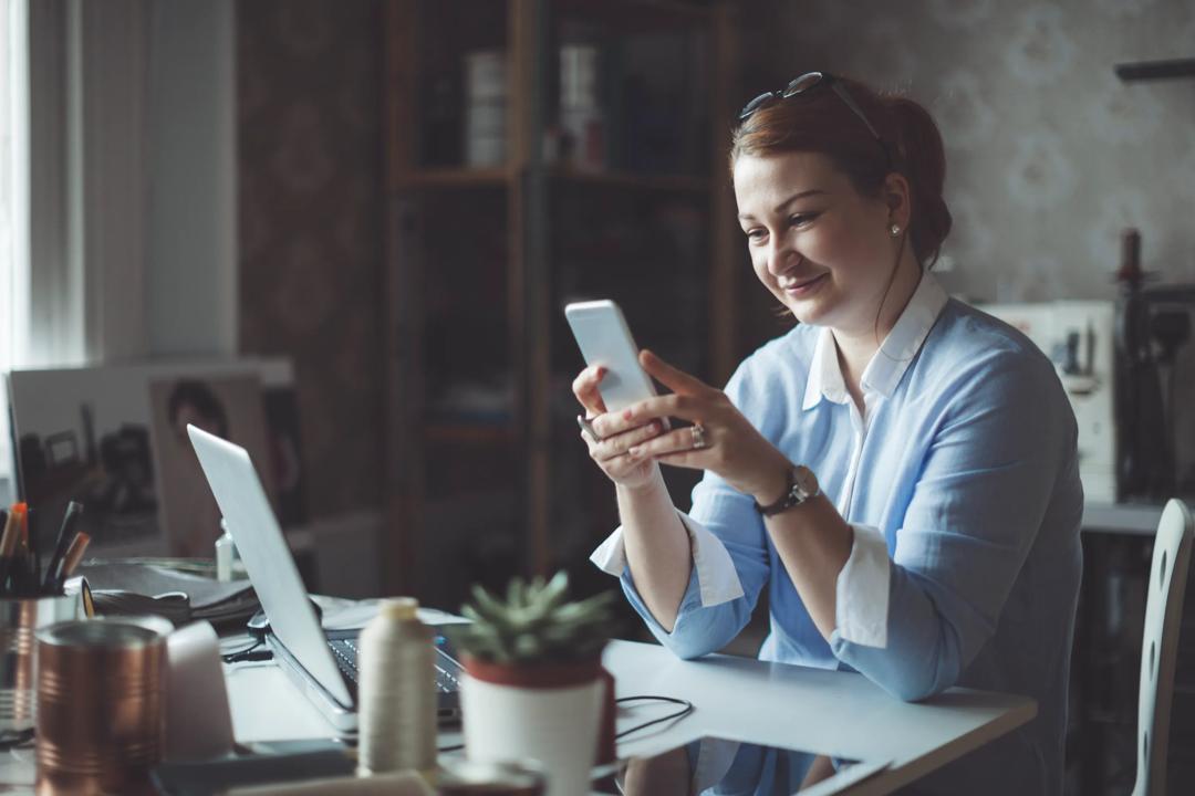 Woman working from her desk at home, using her phone.