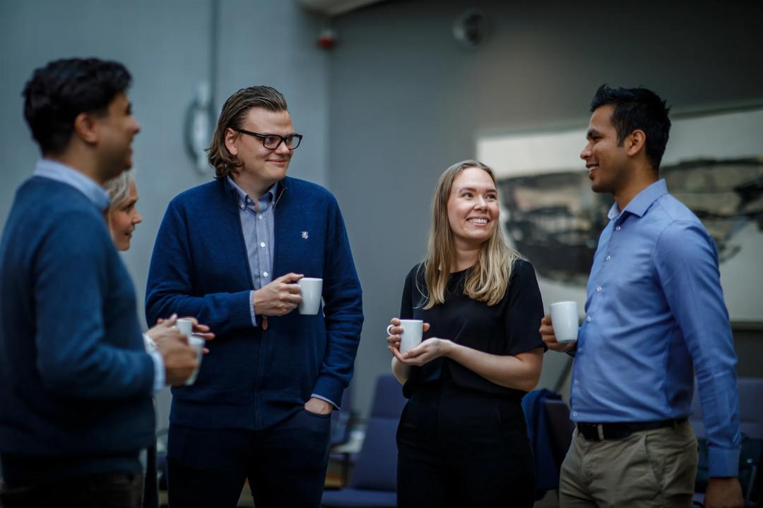 Fire personer som står og mingler med en kopp kaffe i hendene.