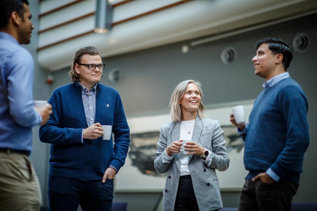 Tre menn og en dame som står og mingler