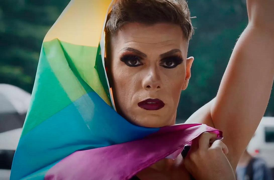 A man with makeup holding a pride flag
