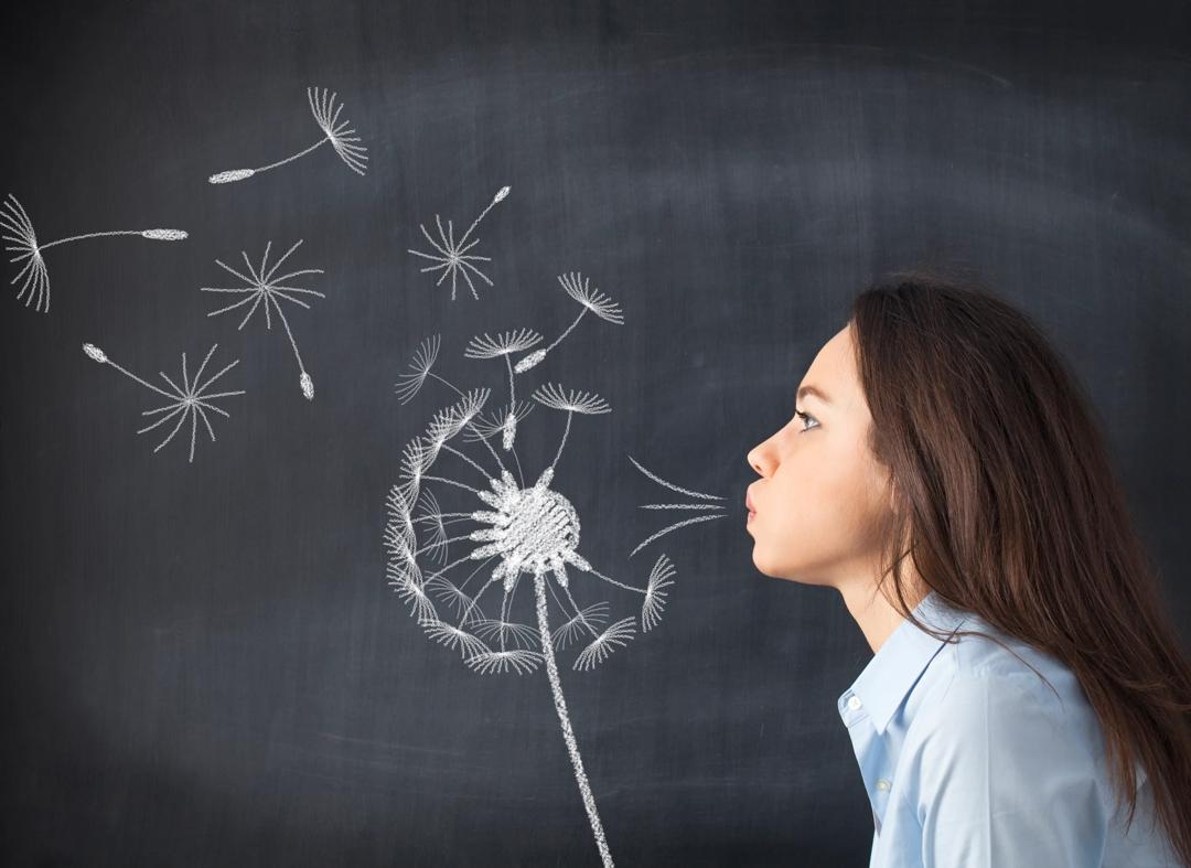 Woman blowing seeds of a dandelion