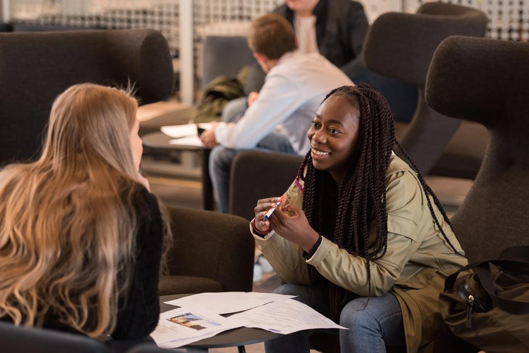 To kvinnelige studenter som sitter å snakker sammen