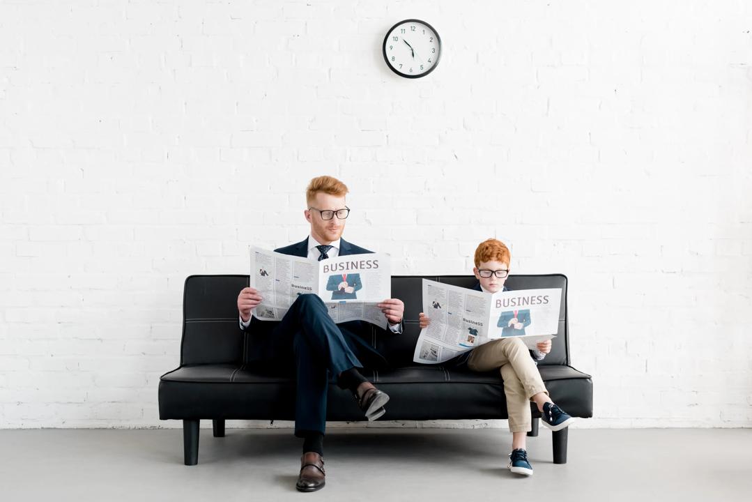 Father and son in suits reading newspaper with the headline "Business"